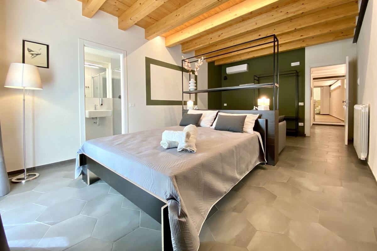 Une chambre moderne avec un grand lit, un plafond en bois, un miroir et une lampe sur pied.