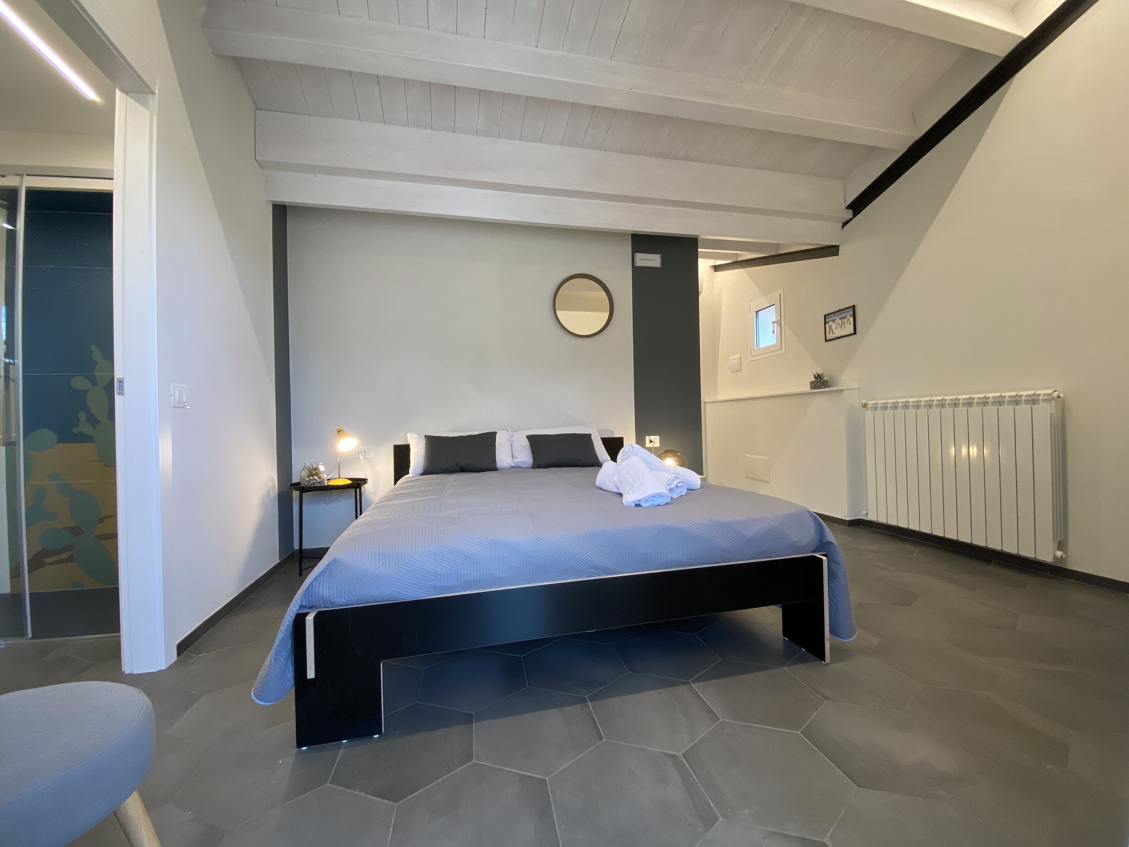 Un dormitorio moderno con una cama grande, una mesita de noche con lámpara, un espejo y un radiador.