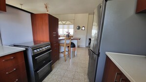 A kitchen with wooden cabinets, a stainless steel refrigerator, a stove, and a dining area with a chair and table. - Beautiful views - walk to restaurants, theaters, First Station, & Old City (Jerusalem)