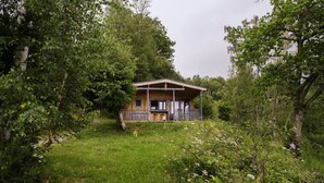 A wooden cabin with a porch, surrounded by lush greenery and trees.