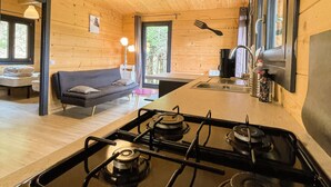 A modern kitchen with wooden walls and a gas stove. There is a sofa and a dining table in the living area.
