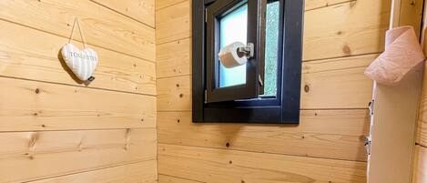 Ein kleines Badezimmer aus Holz mit Toilette, Fenster und einem Toilettenpapierhalter.