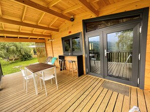 Eine Holzterrasse mit Tisch und Stühlen, einer Bar und einer Glastür, die auf einen Balkon mit Blick ins Freie führt.