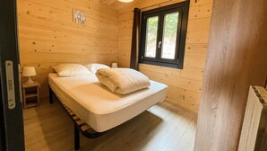 A wooden cabin bedroom with a bed, a nightstand, a window, and a ceiling light.