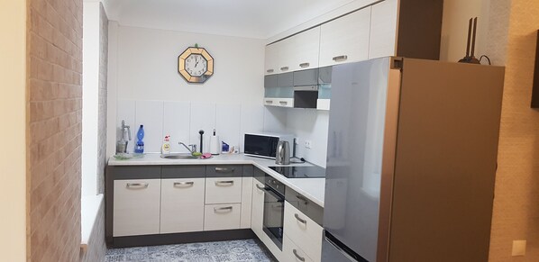 A compact kitchen with white cabinets, a stainless steel refrigerator, a microwave, and a clock on the wall. - Excellent spot in Art Noveau style building close to the river and Old Town (Riga)