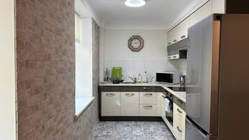 Une cuisine de taille réduite avec un mur en briques, une horloge et un réfrigérateur en acier inoxydable.