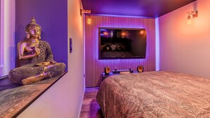 Una habitación con una estatua de Buda, una cama con colcha estampada, un televisor montado en la pared y un techo inclinado.