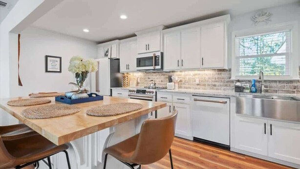 Una cocina moderna con armarios blancos, una mesa de comedor de madera y un microondas empotrado.