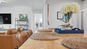 Un comedor moderno con una mesa de madera, individuales tejidos, sillas de cuero y un florero con flores.