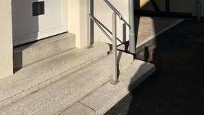 Un edificio con una puerta blanca, un ventanal pequeño y una escalera metálica.
