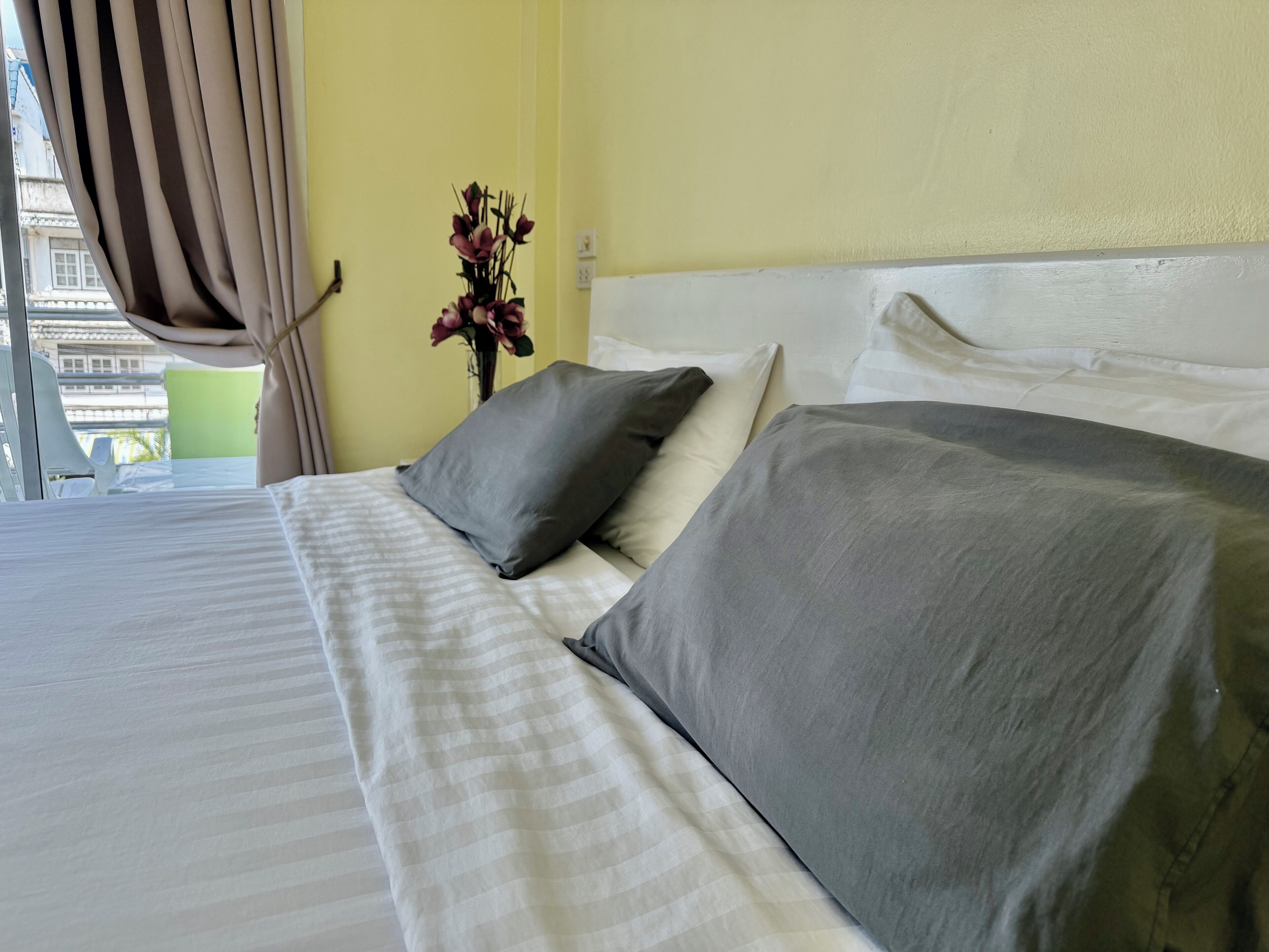 A hotel room with a bed, pillows, a vase with flowers, and a window with curtains.