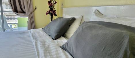 A hotel room with a bed, pillows, a vase with flowers, and a window with curtains.