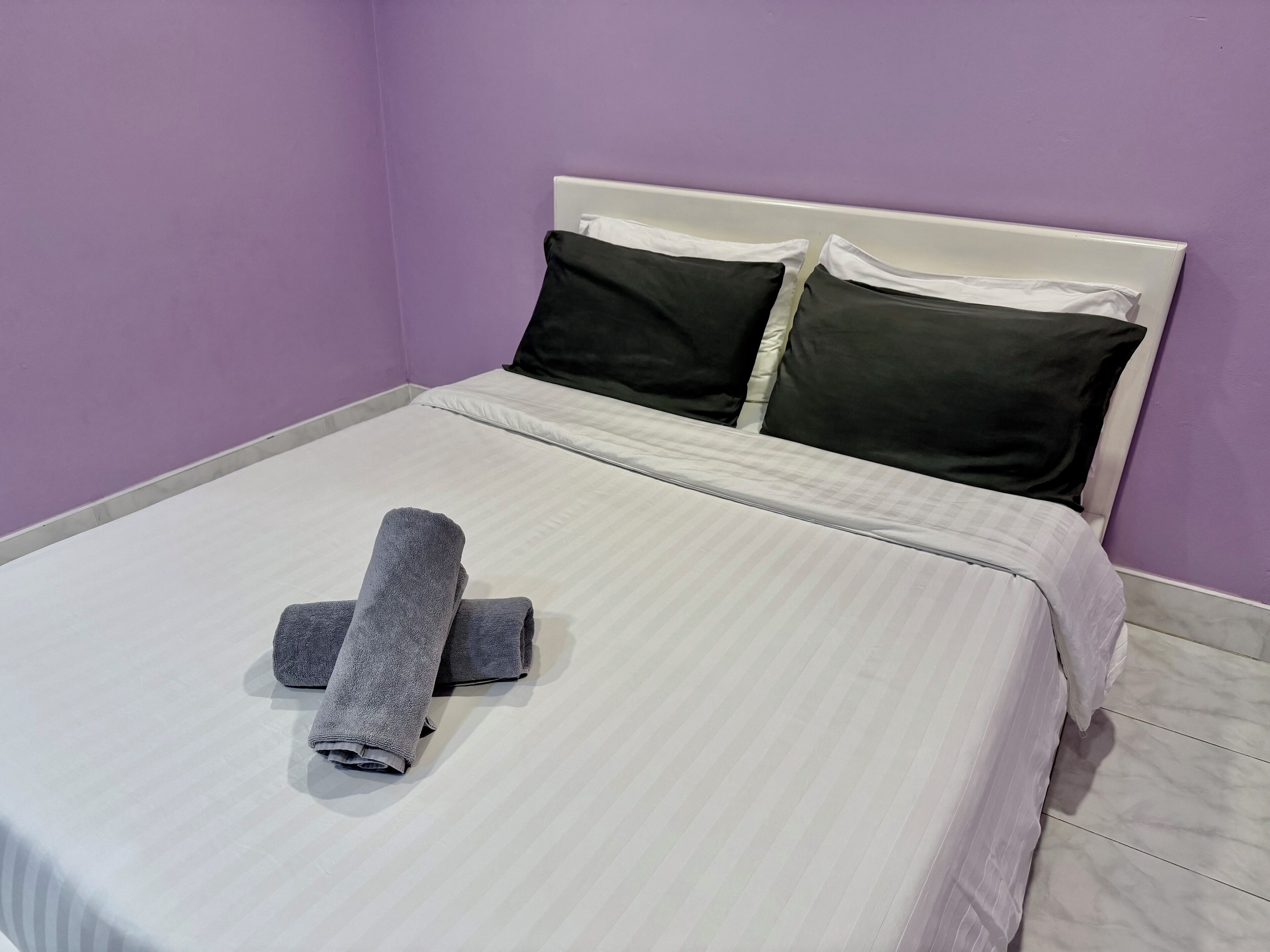 Una cama bien hecha con una colcha a rayas blancas y grises, dos almohadas negras y una toalla gris enrollada sobre la cama.