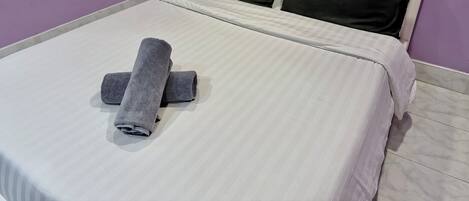 Una cama bien hecha con una colcha a rayas blancas y grises, dos almohadas negras y una toalla gris enrollada sobre la cama.