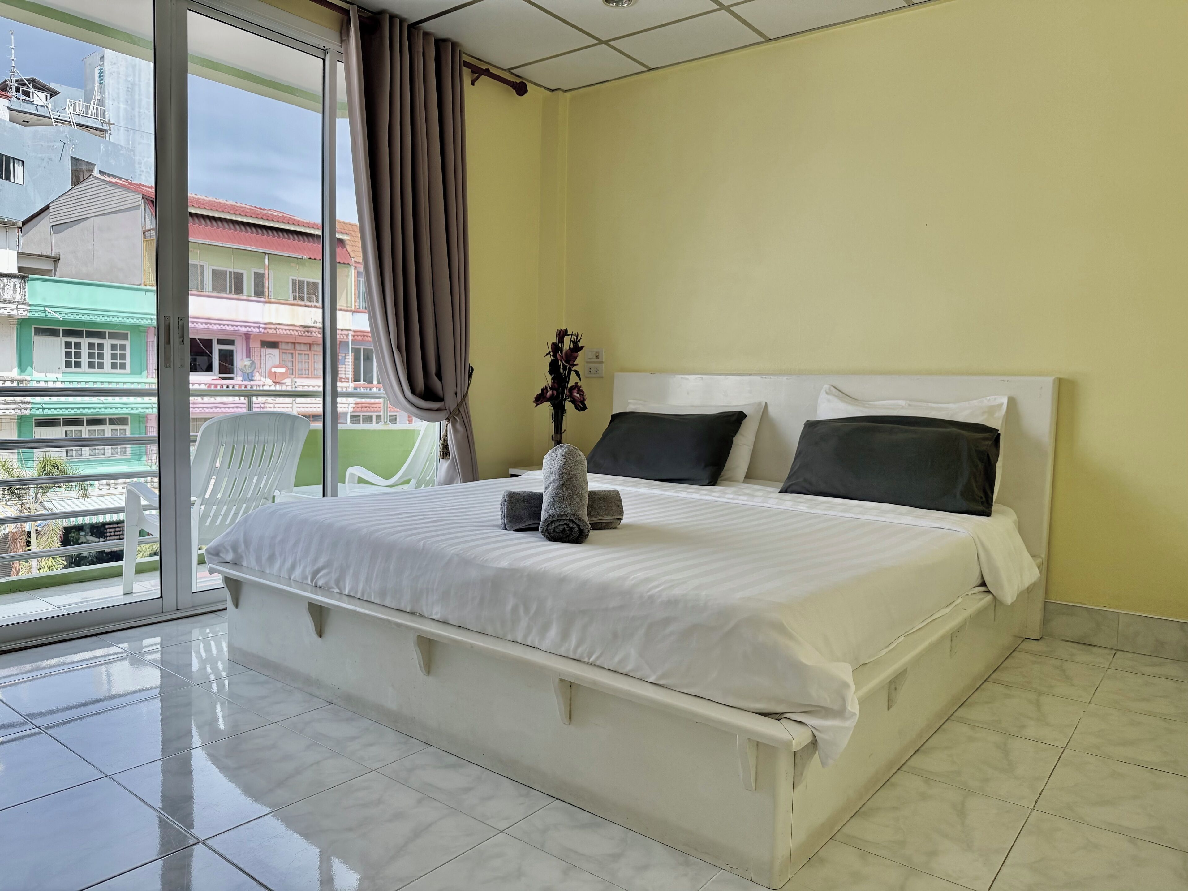 Une chambre d’hôtel avec un lit, une fenêtre avec des rideaux, une chaise et une vue sur les bâtiments environnants.