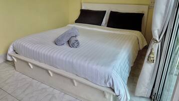 A neatly made bed with a rolled towel, a white headboard, and a window with a curtain.