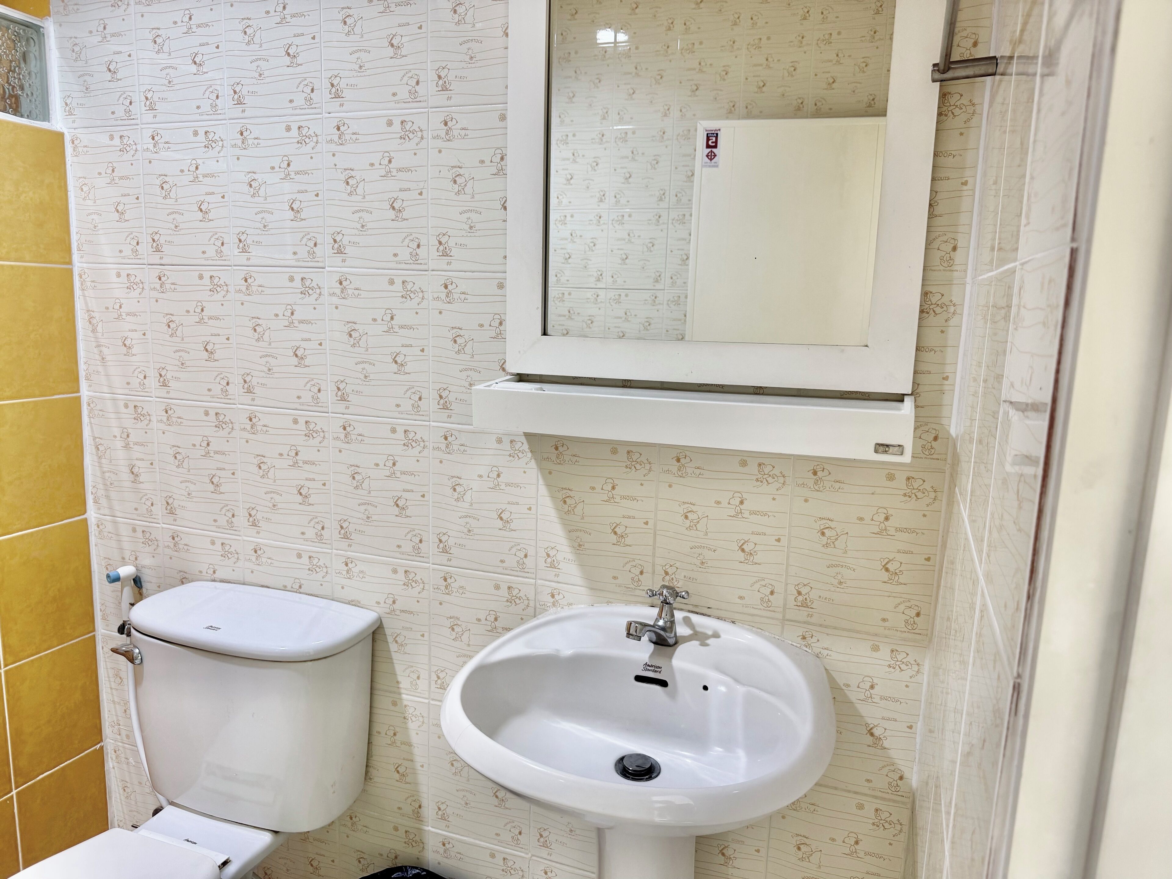 Une salle de bain avec des toilettes, un lavabo et un miroir. Les murs sont recouverts d’un papier peint à motifs.