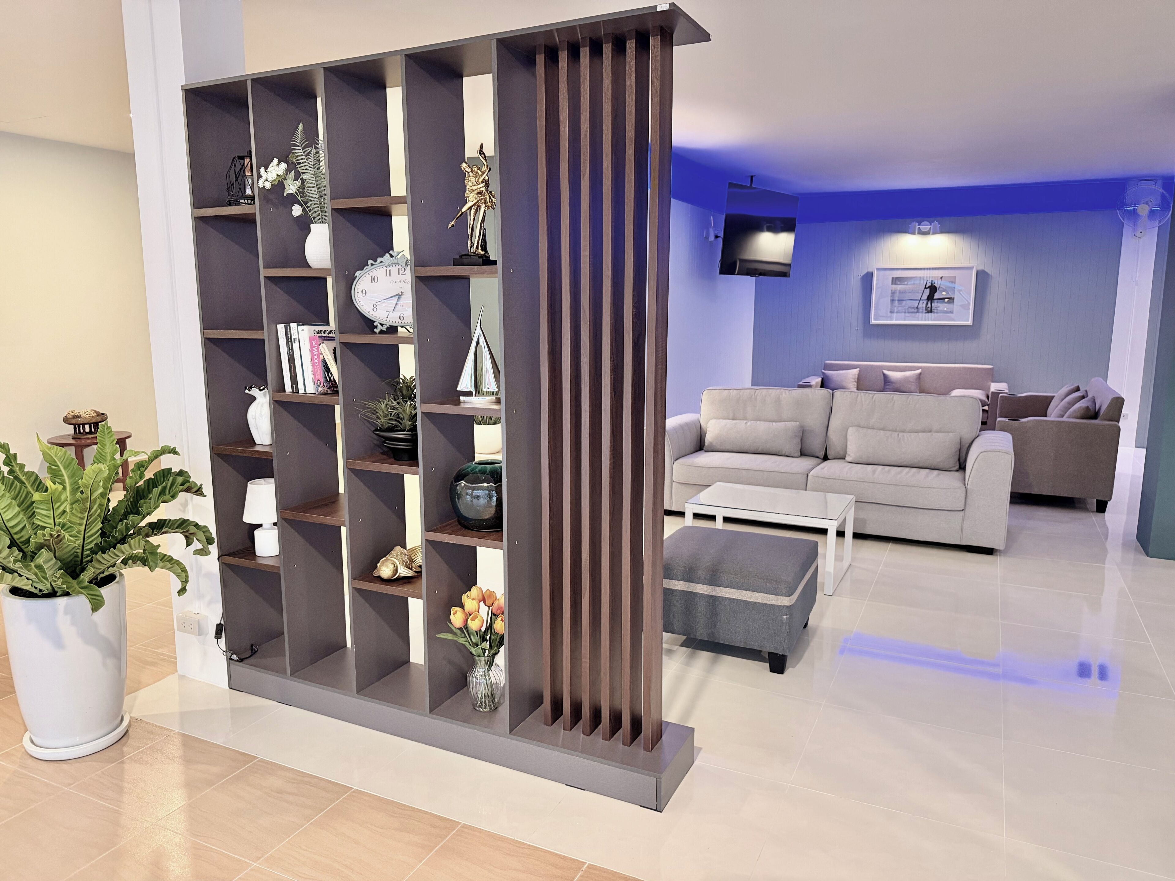 Un salon moderne avec un canapé d’angle, une table basse, une bibliothèque décorative et une plante en pot.