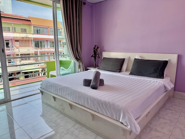 Un dormitorio con una cama grande, una mesita de noche, un jarrón con flores y vistas a edificios a través de una ventana.