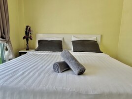 A neatly made bed with white bedding and two dark pillows, a rolled-up gray towel, and a vase with flowers on a bedside table.