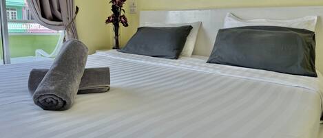 Una cama bien hecha con ropa de cama a rayas, dos almohadas y toallas enrolladas.