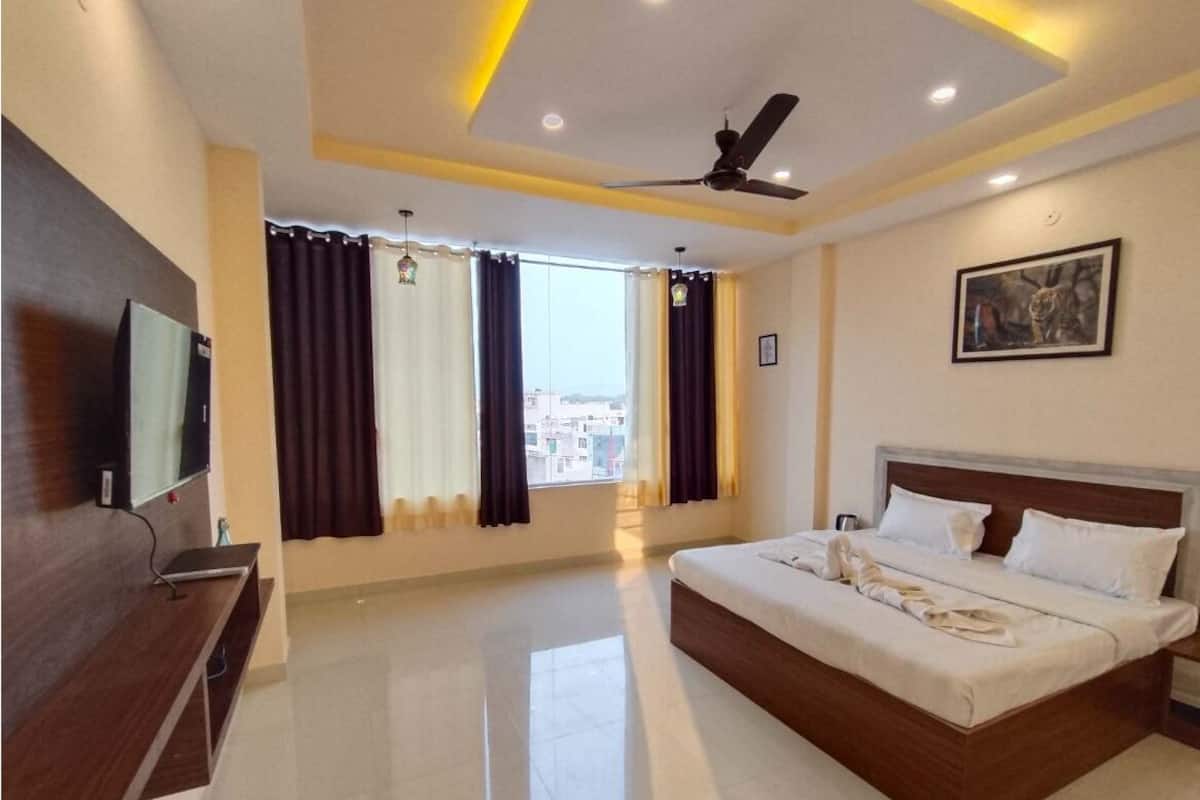 A hotel room with a bed, a TV, a ceiling fan, and a window with curtains.
