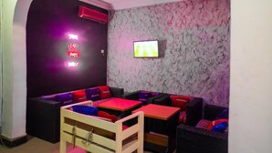 A room with a TV mounted on the wall, a neon sign, and a seating area with tables and chairs. - Royalty Place Hotel (Lagos)