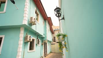 A narrow alleyway between buildings with a light blue facade, a black hanging lamp, and an air conditioning unit.