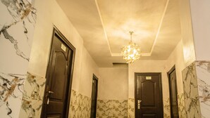 A hallway with marble walls and doors, a chandelier, and a tiled floor. - Royalty Place Hotel (Lagos)