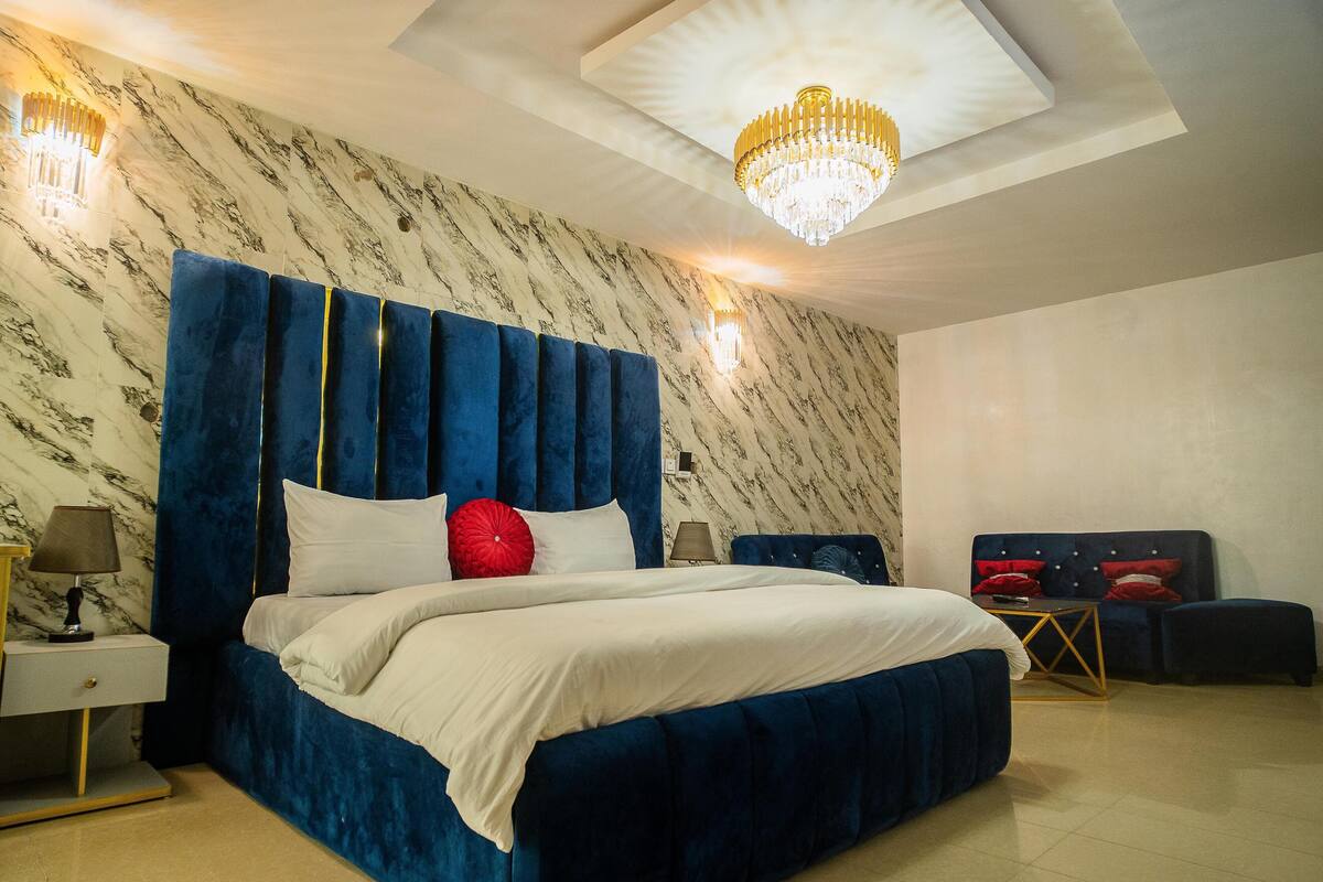 A bedroom with a large bed, marble-patterned walls, a chandelier, and a nightstand with a lamp.