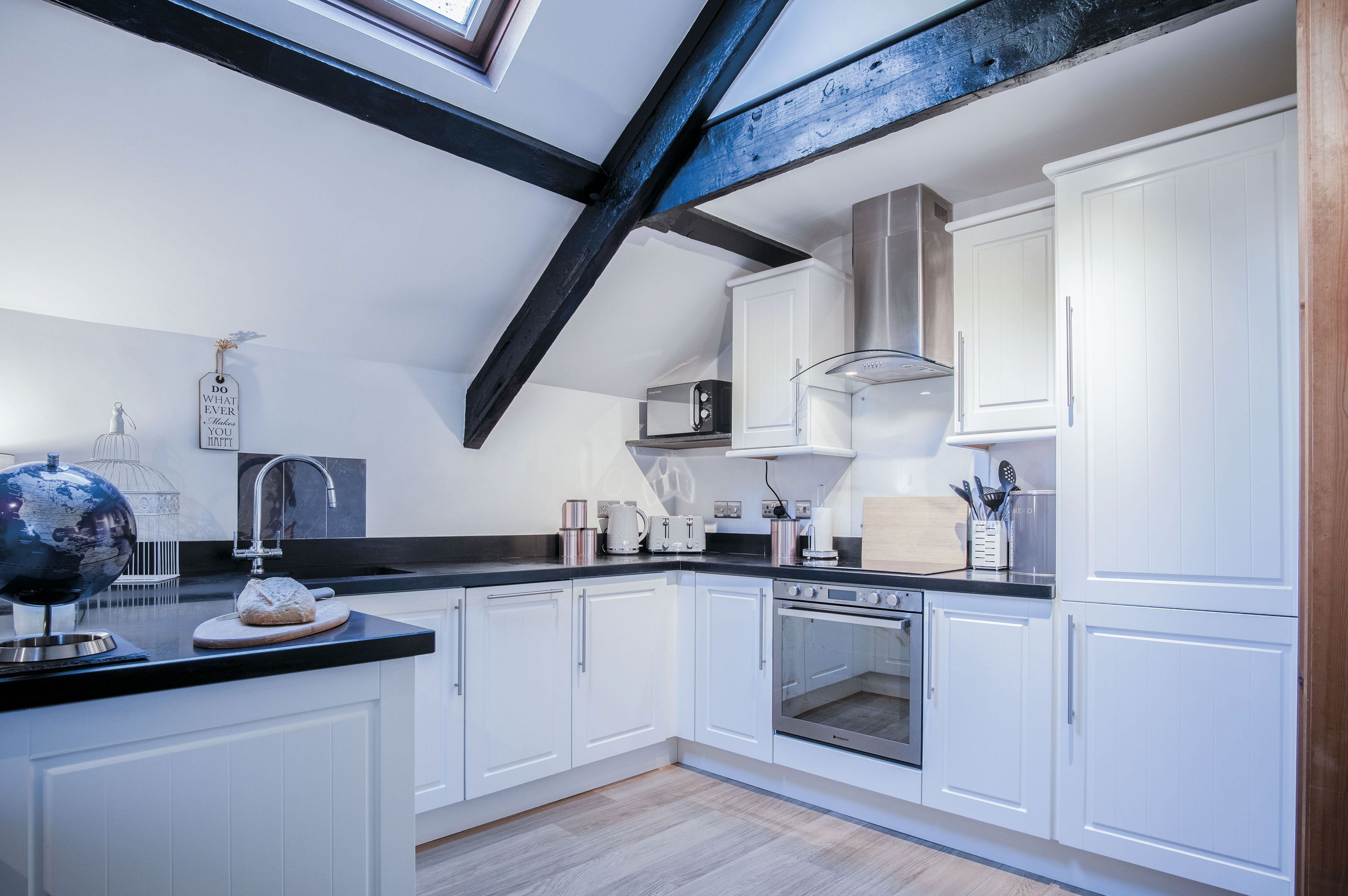 A modern kitchen with white cabinets, a black countertop, and a skylight.