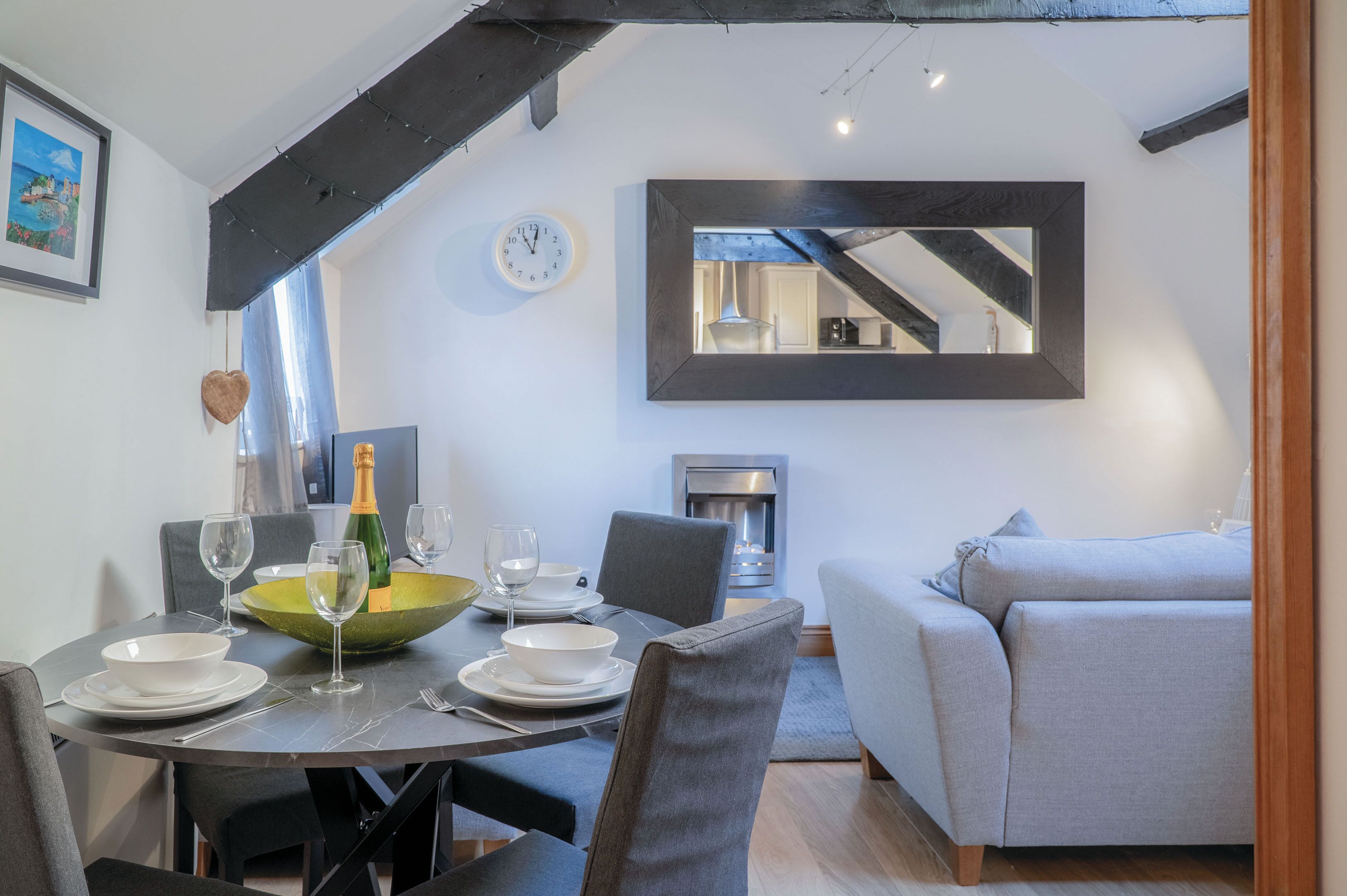 A dining area with a round table, chairs, and a green bowl centerpiece. A clock and a framed mirror are on the walls.