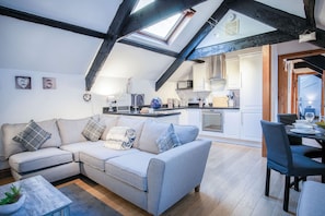 Um loft moderno com vigas aparentes, cama mezanino, cozinha com armários brancos e área de jantar com mesa e cadeiras.