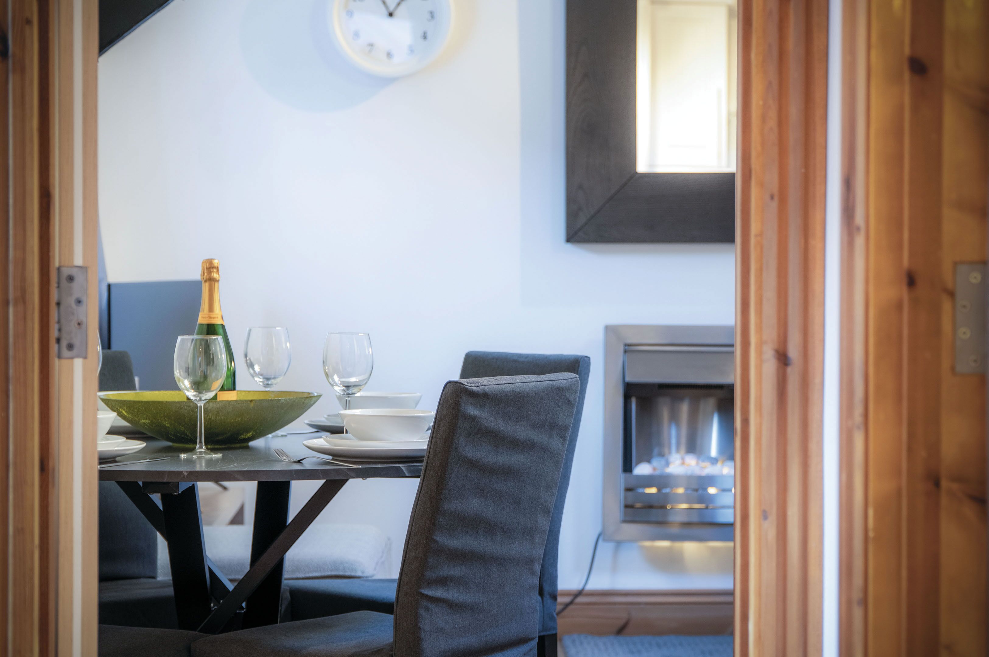 Een eetgedeelte met een tafel gedekt voor twee personen, een groene kom, wijnglazen en een fles champagne.