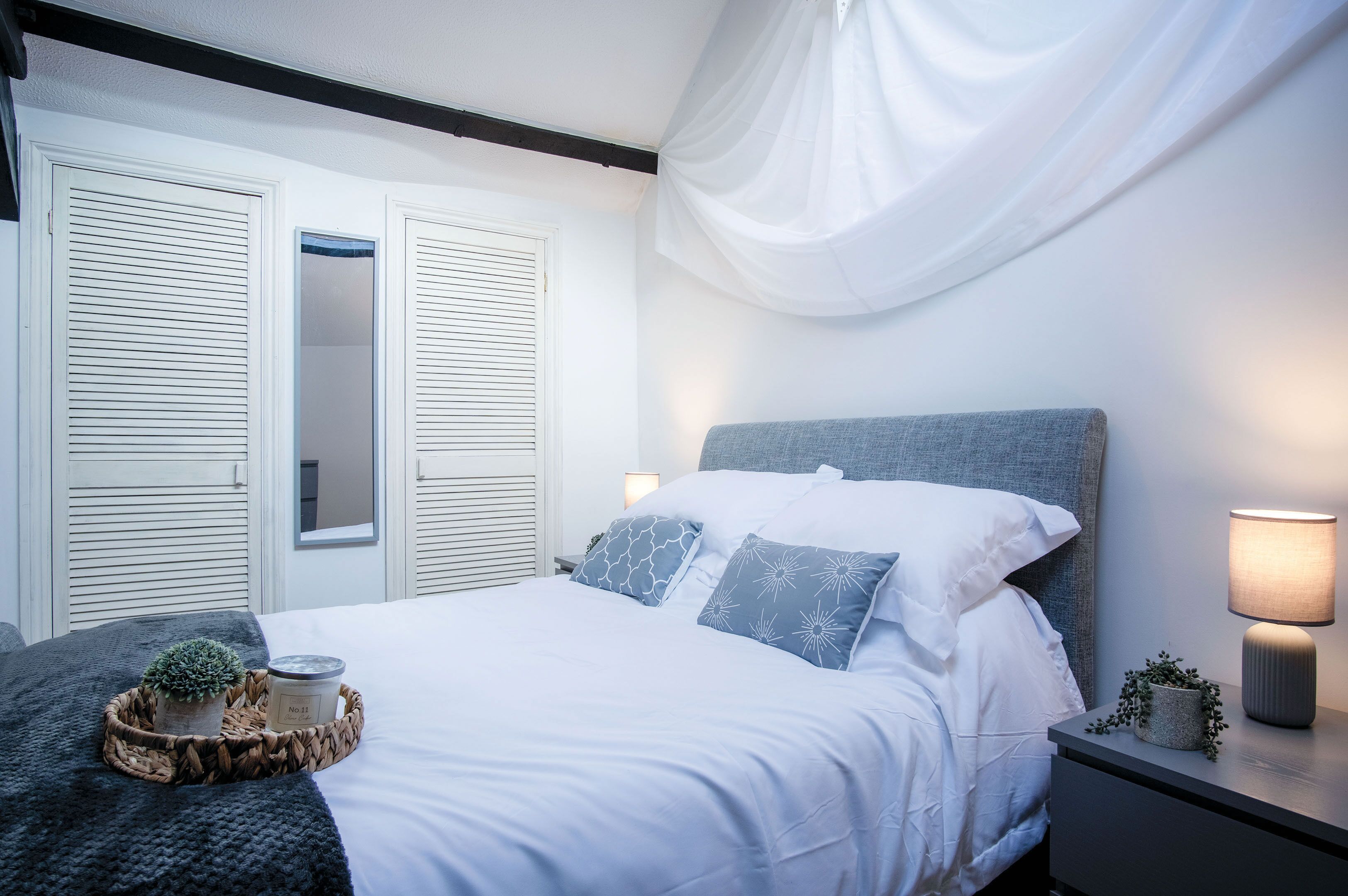 A neatly made bed with white bedding and blue pillows, a bedside lamp, and a small plant on the nightstand.