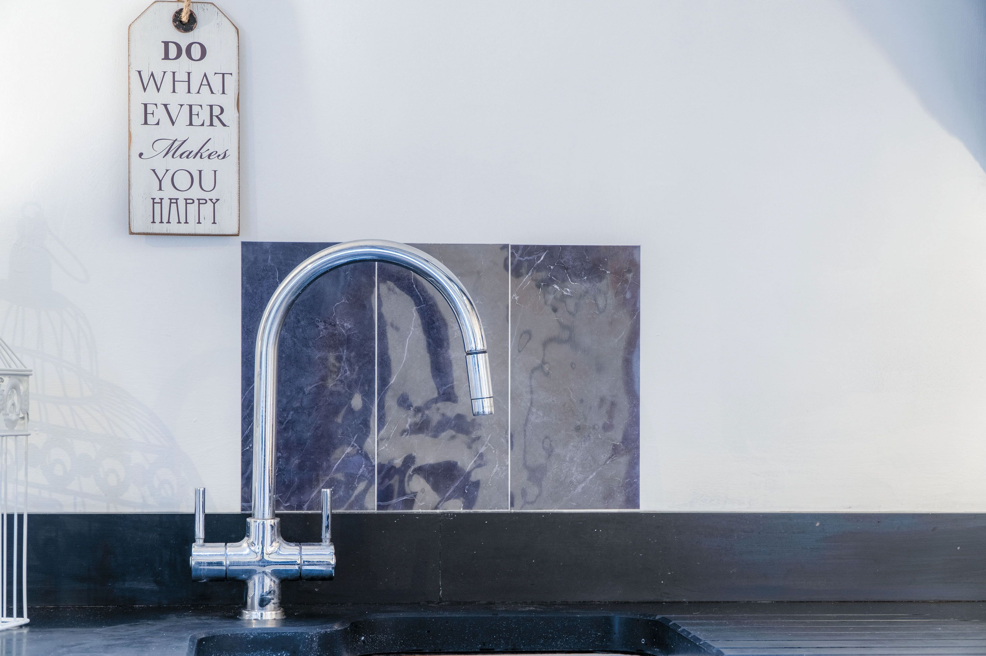 A bathroom with a modern faucet, a decorative sign, and a marble backsplash.