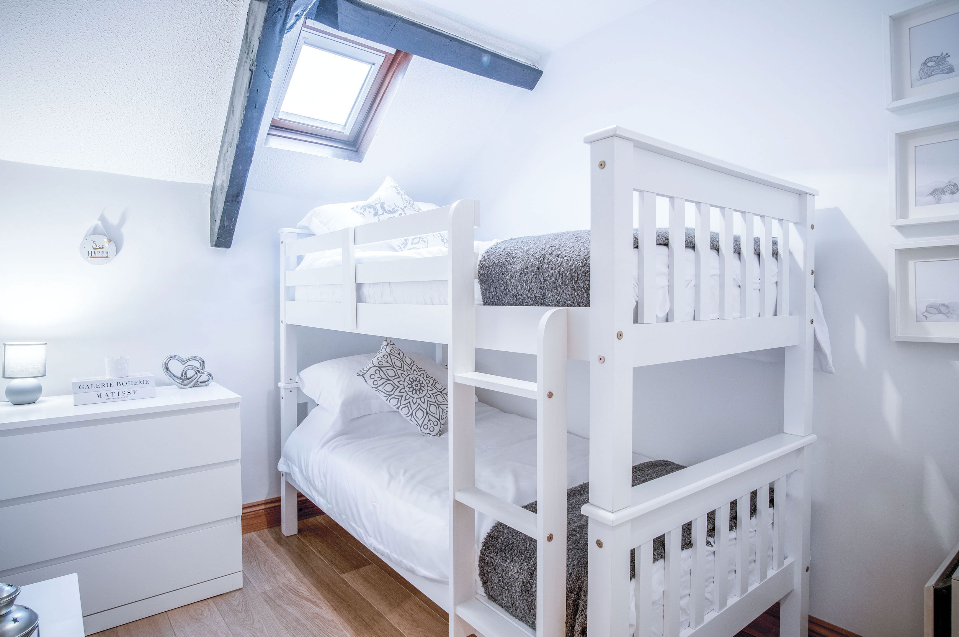 Un lit superposé pour enfant, avec une commode blanche et une petite table placée à côté.