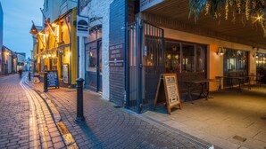Una calle con un restaurante llamado "Tap & Fire Kitchen" con mesas al aire libre y un letrero que anuncia "Hamburguesas Artesanales Desde 2016".
