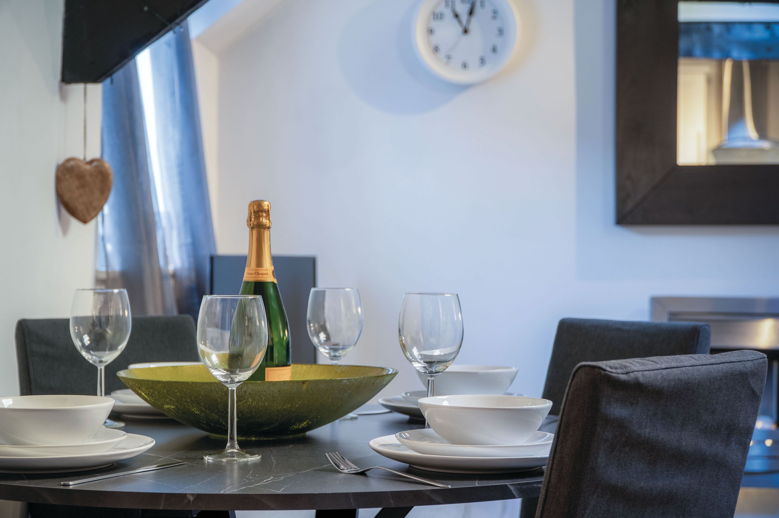 Et spisebord dækket med hvide tallerkner, skåle og vinglas, en grøn skål som midtpunkt og en champagneflaske.