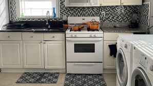 A kitchen with white cabinets, a microwave, a stove with pots, a sink, and a washing machine. - King queen, sweet cozy, and quiet old urban Neighbourhood, charming perfect stay (Birmingham)