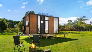 A modern, single-story cabin with a large sliding glass door, a small deck, and a fire pit in the yard. - Bush Retreat 2 by Tiny Away (Alberton West)