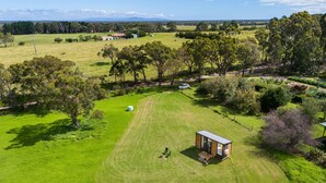 A small, modern cabin with a deck, surrounded by a well-maintained lawn and trees, with a car parked nearby. - Bush Retreat 2 by Tiny Away (Alberton West)
