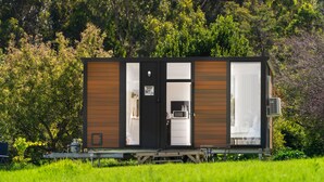 A small, single-story cabin with a sliding door, a small kitchen area, and an air conditioning unit. - Bush Retreat 2 by Tiny Away (Alberton West)