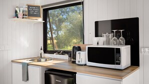 A compact kitchen with a sink, a toaster, a microwave, and a dishwasher. A welcome sign is visible above the window. - Bush Retreat 2 by Tiny Away (Alberton West)