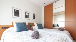 A neatly made bed with a floral bedspread, a rolled towel, and a nightstand with a lamp and a small plant. - Casa cerca BCN,  ideal empresas, 15min FiraBCN, A/C (Sant Boi de Llobregat)