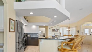 A modern kitchen with stainless steel appliances, a central island with bar stools, and a dining area with wicker chairs. - Tranquility with Divine Sunsets in Vacation Land -Sleeps 8 -Pet Friendly (Punta Gorda)