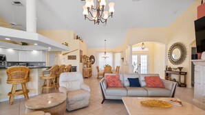 A spacious living room with a large grey sofa, a beige armchair, and a round coffee table. There is a kitchen area with white cabinets and a dining table with chairs. - Tranquility with Divine Sunsets in Vacation Land -Sleeps 8 -Pet Friendly (Punta Gorda)