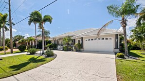 A residential driveway leading to a house with a garage, surrounded by palm trees and well-maintained lawns. - Tranquility with Divine Sunsets in Vacation Land -Sleeps 8 -Pet Friendly (Punta Gorda)