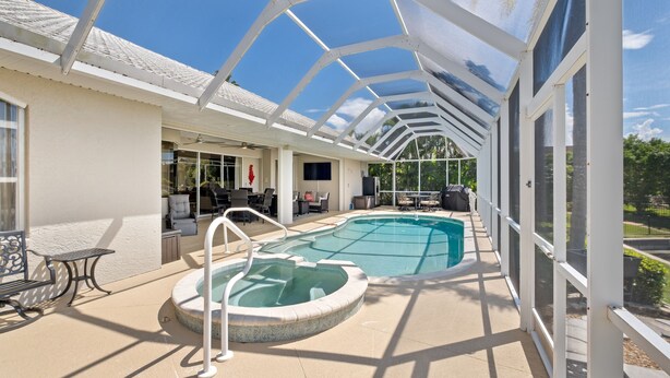 A covered outdoor swimming pool with a hot tub, surrounded by lounge chairs and a patio area. - Tranquility with Divine Sunsets in Vacation Land -Sleeps 8 -Pet Friendly (Punta Gorda)