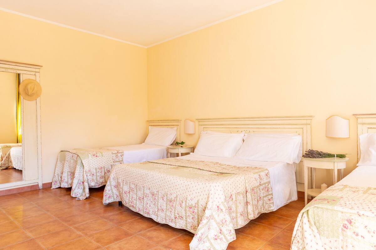 A hotel room with two single beds, a large bed, and a mirror.